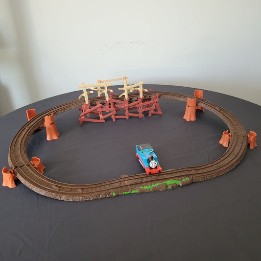 Das vollständige Thomas und seine Freunde Shake, Shake Bridge Playset, bestehend aus der Brücke, den dazugehörigen Schienen und der Lokomotive Thomas. Das Set ist auf einem schwarzen Untergrund arrangiert, während der Hintergrund weiß ist, wodurch die einzelnen Elemente besonders gut zur Geltung kommen.