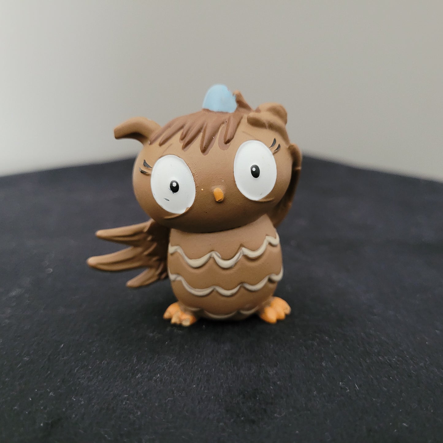 Tonie / Tonies Figur die Eule mit der Beule. Zu sehen ist die Vorderseite auf schwarzer Oberfläche und grauem Hintergrund.