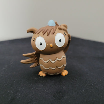 Tonie / Tonies Figur die Eule mit der Beule. Zu sehen ist die Vorderseite auf schwarzer Oberfläche und grauem Hintergrund.