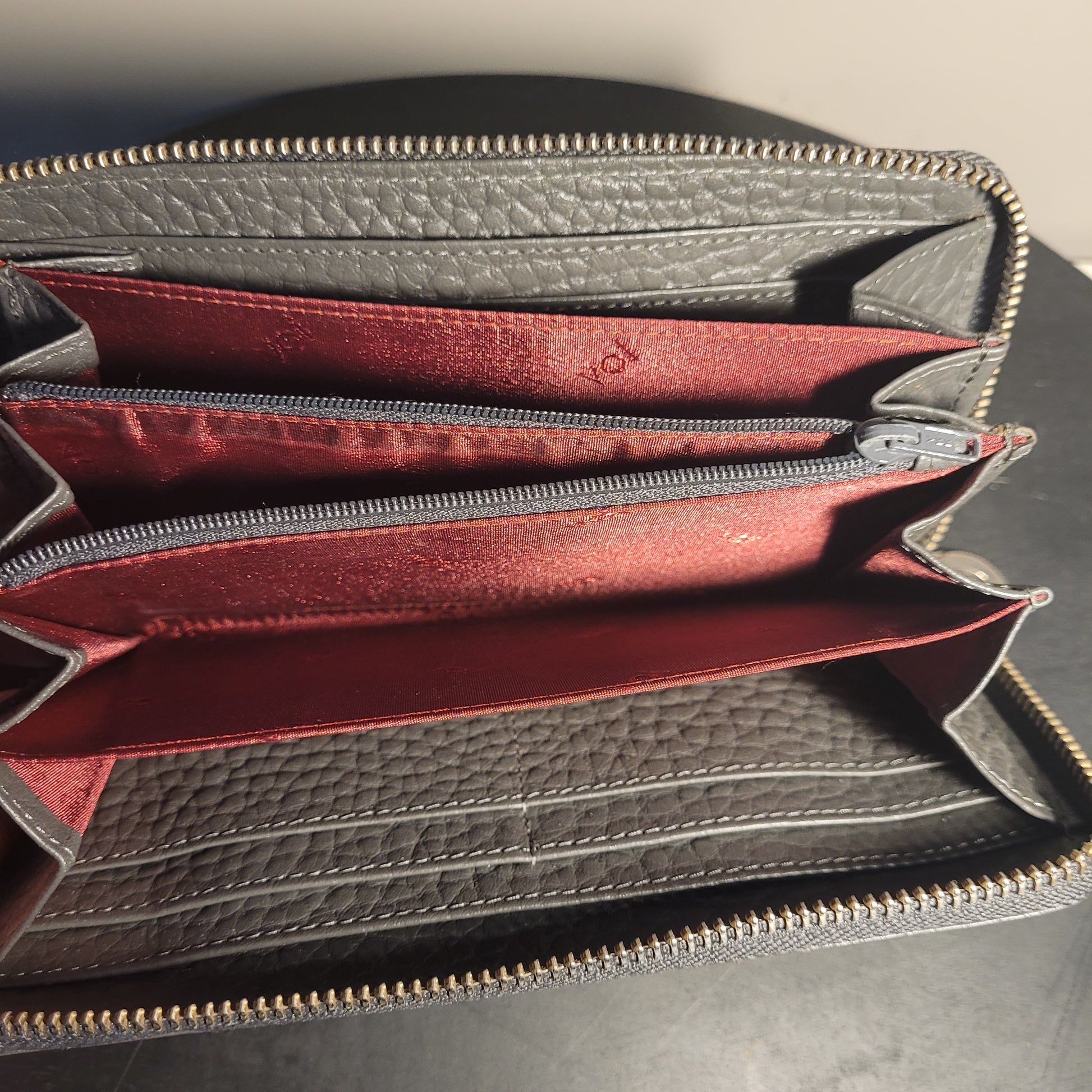 Geöffnete schwarze Leder-Geldbörse von Voi mit rotem Innenfutter, mehreren Kartenfächern und einem grauen Reißverschlussfach, präsentiert auf dunklem Hintergrund.