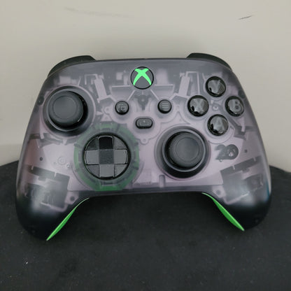 Das Bild zeigt die Vorderansicht des Xbox Wireless Controller – 20th Anniversary Special Edition. Erkennbar sind das transparente, rauchgraue Gehäuse mit sichtbaren Innenkomponenten, schwarze Bedienelemente wie Joysticks, D-Pad und Tasten (A, B, X, Y), sowie die grün leuchtende Xbox-Taste mittig. Die grünen Akzente an den Griffen und die klassische Formgebung unterstreichen den Gaming-Charakter und den Jubiläumsstil des Controllers. Der Zustand wirkt gepflegt.