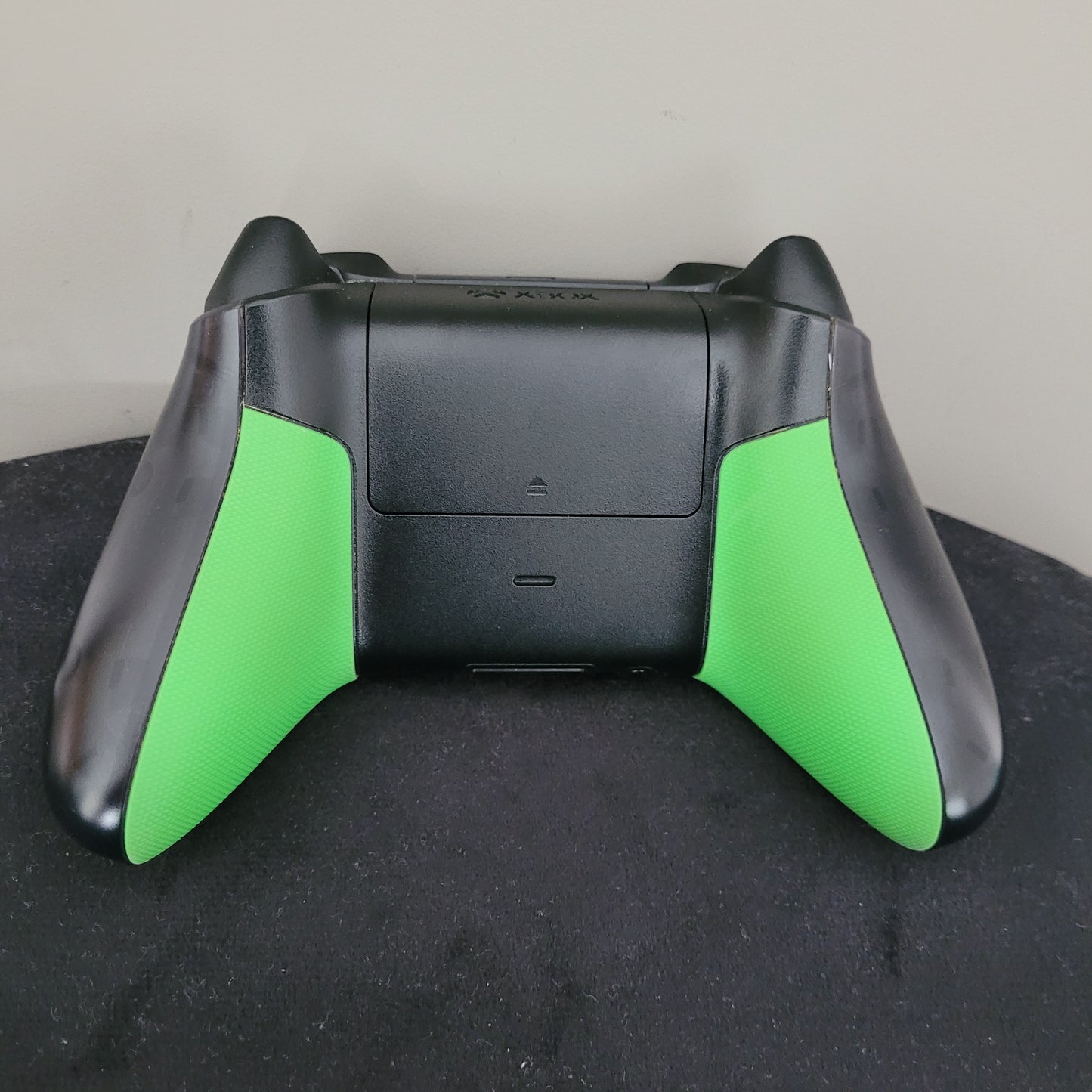 Die Rückseite des Controllers zeigt ein schlankes, ergonomisches Design mit griffigen, grün gefärbten Seitenelementen, die einen sicheren Halt bieten. Zentral befindet sich das Batteriefach mit einem kleinen Pfeil, der die Öffnungsrichtung kennzeichnet. Die beiden Schultertasten am oberen Rand sind gut sichtbar und leicht zugänglich, was für präzise Steuerung bei intensiven Gaming-Sessions sorgt.