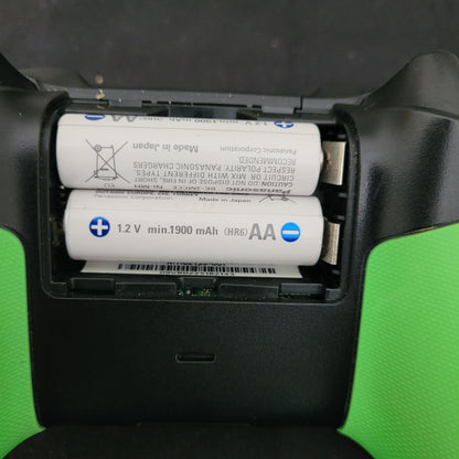 Das Bild zeigt das geöffnete Batteriefach des Xbox Wireless Controllers – 20th Anniversary Special Edition. Darin befinden sich zwei weiße AA-Batterien der Marke Panasonic mit folgender Kennzeichnung: „1.2V min. 1900 mAh (HR6) AA – Made in Japan“. Auf den Batterien sind zudem Sicherheitshinweise zu sehen, darunter: „Nicht ins Feuer werfen“, „Nicht mit verschiedenen Batterietypen mischen“ und „Nur mit dafür vorgesehenen Ladegeräten aufladen“.