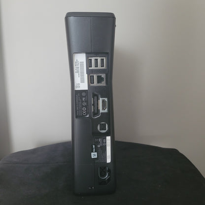 Xbox 360 S Modell 1439 – Rückseite auf schwarzem Untergrund und weißem Hintergrund Das Bild zeigt die Rückseite einer Xbox 360 S Modell 1439, platziert auf einem schwarzen Untergrund mit einem weißen Hintergrund. Sichtbar sind die verschiedenen Anschlüsse der Konsole, darunter HDMI, USB-Ports, Netzteilanschluss und AV-Ausgang. Das schlanke Design und die Lüftungsschlitze an der Rückseite unterstreichen die für die Xbox 360 S typische Bauweise.