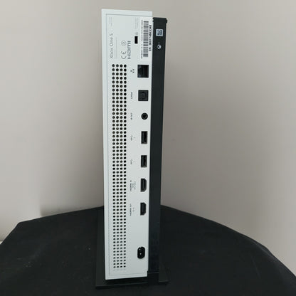 Das Foto zeigt die Rückseite einer weißen Xbox One S Konsole. Sichtbar sind mehrere Anschlüsse in einer horizontalen Reihe: darunter Ethernet, S/PDIF, IR-Out, zwei USB-Ports, HDMI-In, HDMI-Out sowie der Stromanschluss. Über den Ports befindet sich ein Seriennummer-Aufkleber („SN: 369717665346“), darunter ist ein längliches Lüftungsgitter integriert. Links unten sind das Xbox One S Logo, das HDMI-Emblem und diverse Zertifizierungszeichen zu erkennen. 