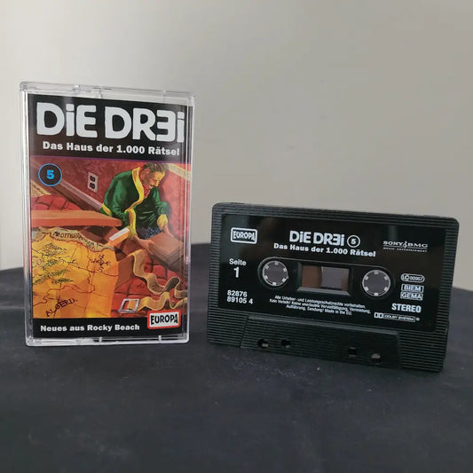 Schwarze Hörspielkassette und Originalhülle von Die Dr3i – Folge 5: Das Haus der 1.000 Rätsel.
