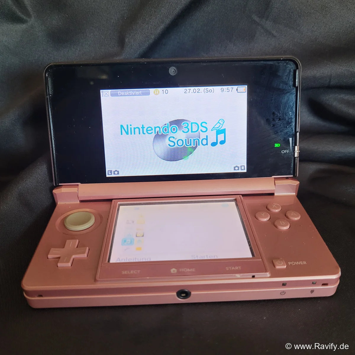 Nintendo 3DS XL Konsole in Pink und Rosa geöffnet auf Stoffhintergrund.