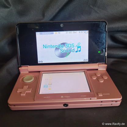 Nintendo 3DS XL Konsole in Pink und Rosa geöffnet auf Stoffhintergrund.