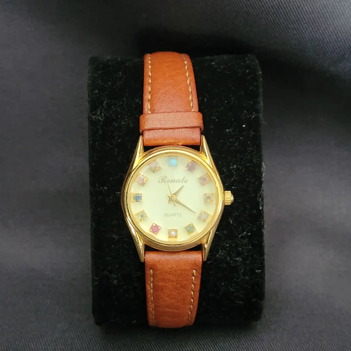 Elegante Vintage Renato Quartz Damen-Armbanduhr in Goldoptik mit zwölf verschiedenen, bunten Edelsteinen als Stundenmarkierungen und einem braunen Artisan-Lederarmband.