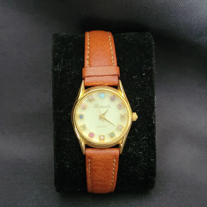 Elegante Vintage Renato Quartz Damen-Armbanduhr in Goldoptik mit zwölf verschiedenen, bunten Edelsteinen als Stundenmarkierungen und einem braunen Artisan-Lederarmband.