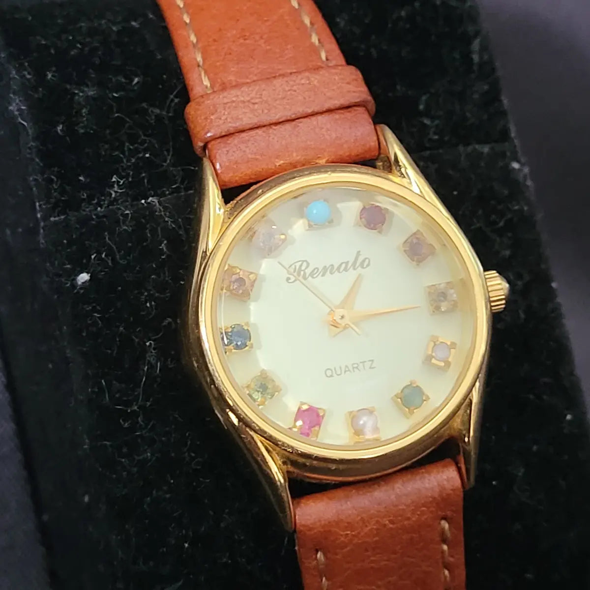 Elegante Vintage Renato Quartz Damen-Armbanduhr in Goldoptik mit zwölf verschiedenen, bunten Edelsteinen als Stundenmarkierungen und einem braunen Artisan-Lederarmband.